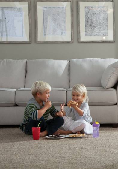Young blonde brother and sister sitting on a plush living room carpet eating cookies